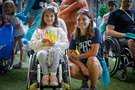 a girl in a wheelchair with a woman squatting beside her